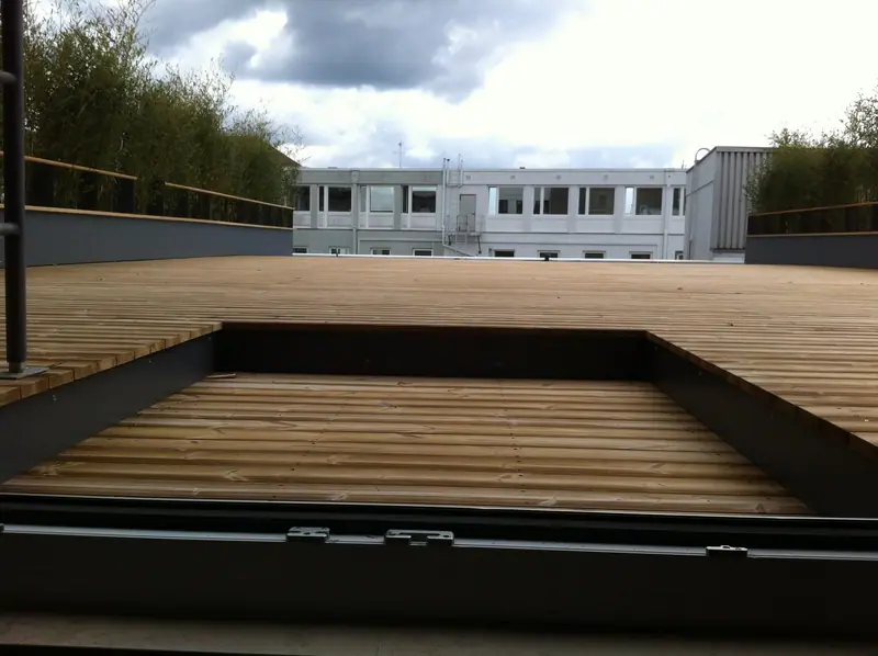Terrassenfläche mit Holzdielen neben einer Öffnung im Boden, dahinter Bambus und Himmel